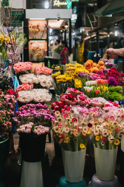 A vibrant floral market stall in Rayners Lane displaying an extensive selection of fresh flowers arranged in various bouquets and bouquets, including pink roses, white peonies, yellow chrysanthemums, 