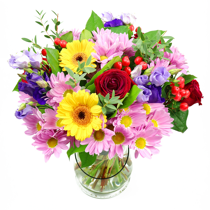 A vivid mixed-flower arrangement stands proudly in a clear glass vase, the entire composition captured against a clean white backdrop that lets each blossom and leaf feel distinct, as if you were leaning in to examine it on a Rayners Lane windowsill. At the heart of the bouquet, deep red roses create an immediate focal point, their velvety petals unfurling in tight spirals that speak of affection and a hint of classic romance. Ringing them are golden yellow gerbera daisies with dark brown-orange centres, their broad, flat faces turning outward like small suns, spreading a bright, confident mood that would lift any living room from Rayners Lane to South Harrow. Generous tufts of soft pink daisies or chrysanthemums surround these stronger colours, each bloom a constellation of fine petals around a tiny yellow centre, filling out the arrangement and adding a tender, pastel balance. Threaded between these more familiar shapes are stems of purple and lavender lisianthus, their bell-shaped blooms and gently ruffled edges bending this way and that, creating interesting pockets of light and shadow. Small sprays of glossy red hypericum berries punctuate the petals, perfectly round and smooth, providing a modern, textural twist. Supporting all of this is a varied bed of greenery: broad, dark leaves forming a rich base and lighter, more feathery foliage reaching upward, giving the bouquet an organic, freshly gathered appearance. The clear glass vase reveals the tidy stems and transparent water, hinting at professional skill and same-day preparation by local florists who know the Rayners Lane neighbourhood well. Together, the colours and textures convey a feeling of joy, gratitude, and celebration, making this arrangement suitable for birthdays, thank-you gestures, housewarmings, or simply bringing a burst of floral happiness into an ordinary day.